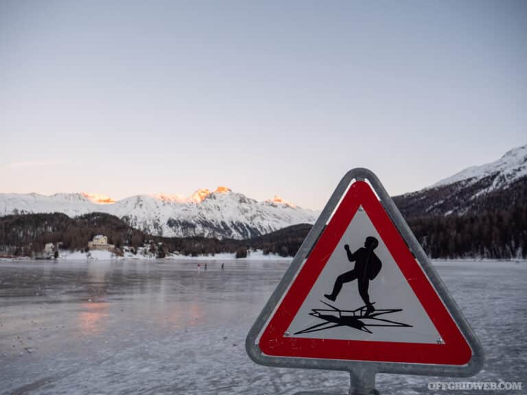 A triangular warning sign that indicates the potential danger of falling through ice next to a frozen mountain lake, to help mitigate cold water safety.