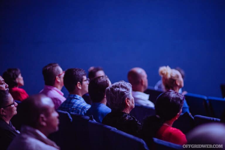 Photo of an audience paying attention to a lecture in a darkened lecture hall.