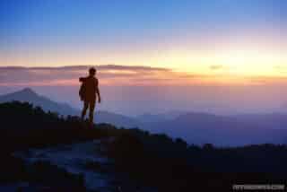 Silhouette of man going it alone with a backpack at mountain top on background of sunset mountains.