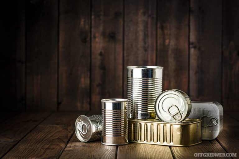 Studio photo of a a pile of unlabeled soup cans stacked on a wooden floor.