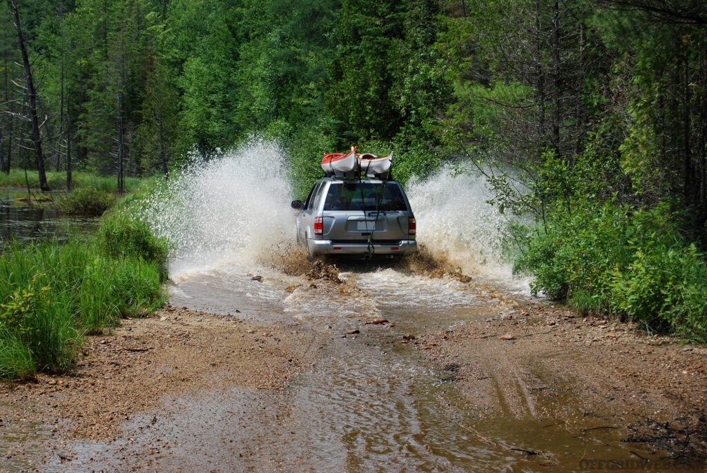 Photo of an SUV driving down a water logged forest trail.