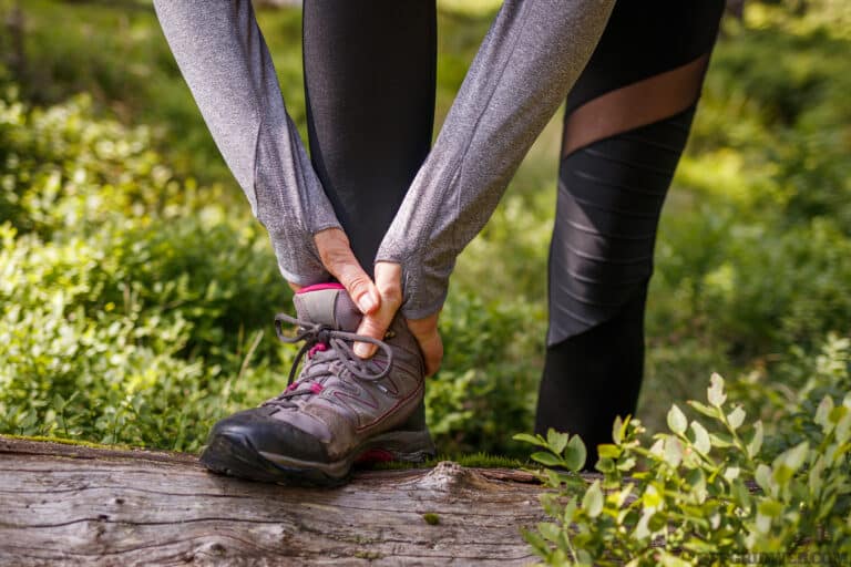 Sprain ankle during hiking in nature. Woman feeling pain after accident injury outdoors.