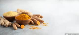 Turmeric and ginger powder in wooden bowl and fresh turmeric root on grey concrete background. Banner with copy space.