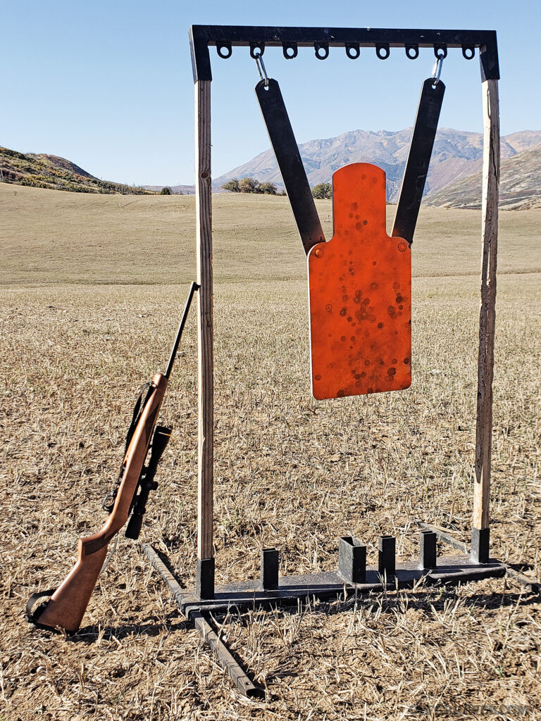Photo of a steel silhouette target, with a survival rifle propped next to i.