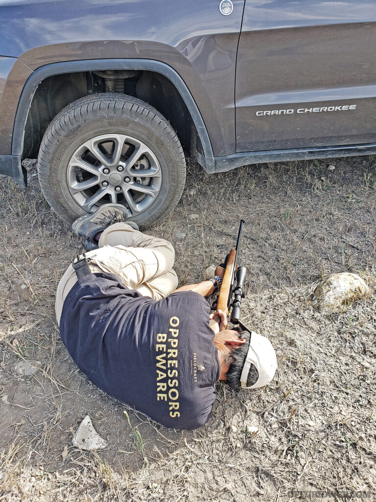 Photo of a man aiming under a vehicle.