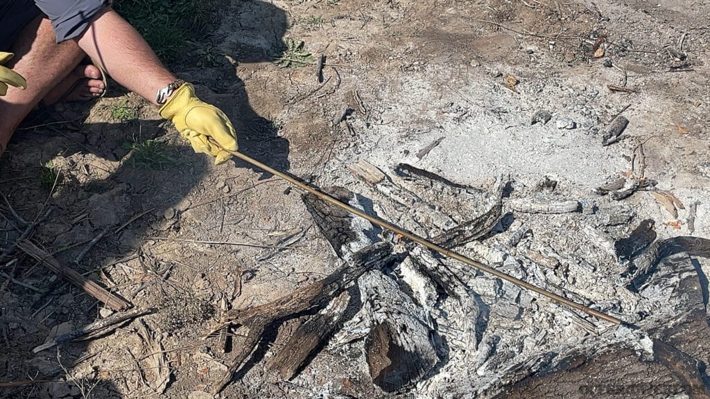 Photo of a student using the heat of a fire to loosen bamboo fibers enough to straighten it.