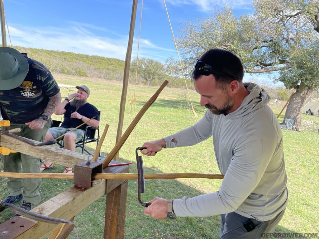 Photo of a Primitive Wilderness Survival student using a draw knife to sculpt their bow.