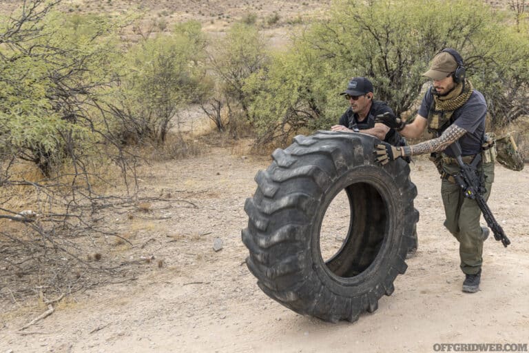Photo of a man with tactical gear pushing a large tire.