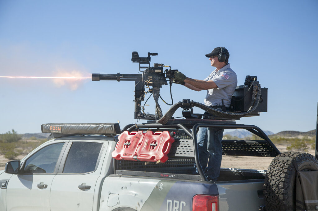 Photo of a man shooting a Dillon Aero minigun mounted to the top of a ford ranger.
