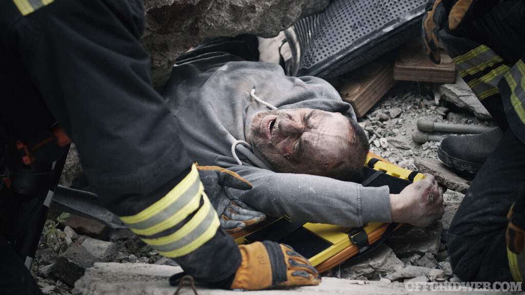 From above senior man lying on spinal board and talking with emergency service workers during rescue mission on remains of demolished building
