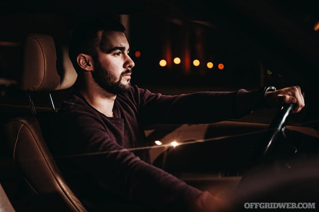 Photo of a man behind the wheel, driving down a dark street at night.