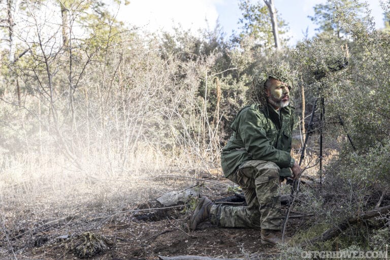 Photo of a camouflaged man kneeling in the brush.