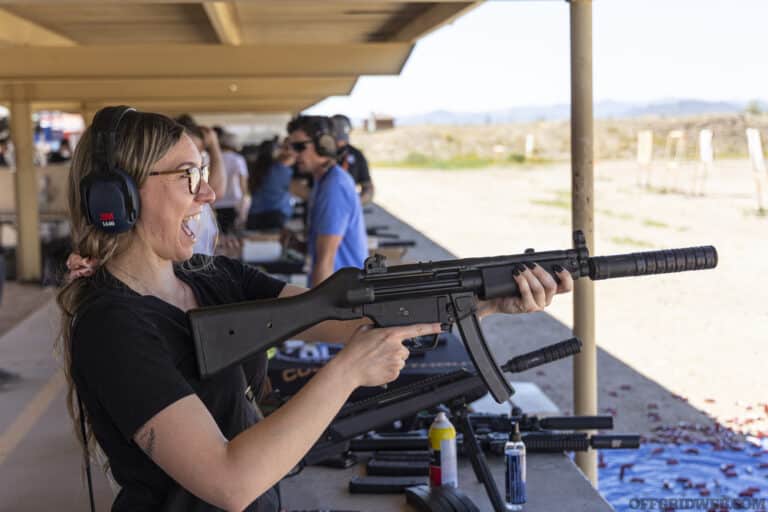 Photo of an adult woman at range very excited to be shooting a firearm with a silencer.