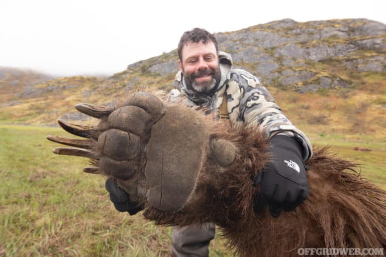 Photo of an adult male hunter holding up the massive paw of a recently harvested brown bear.