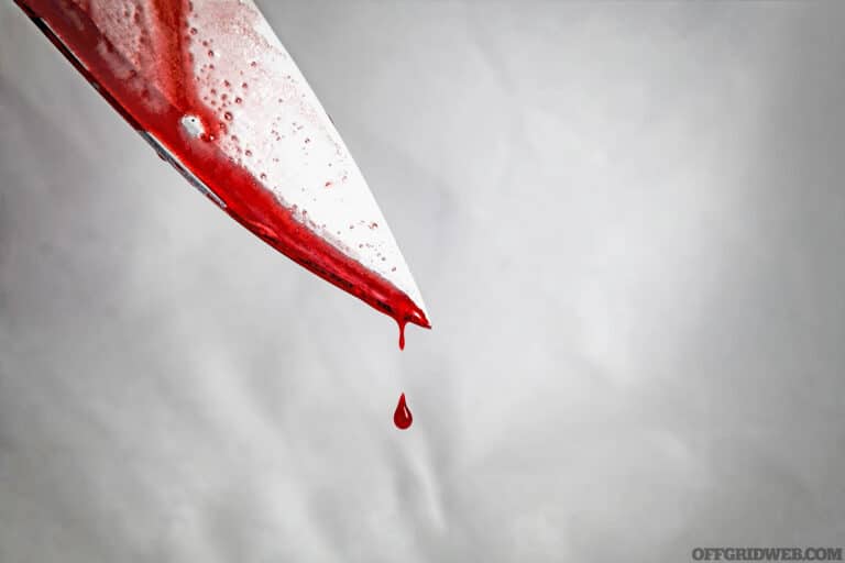 close-up of man holding knife smeared with blood and still dripping.